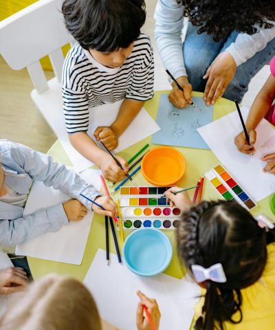 Top view of children painting with watercolors at a preschool art class.
